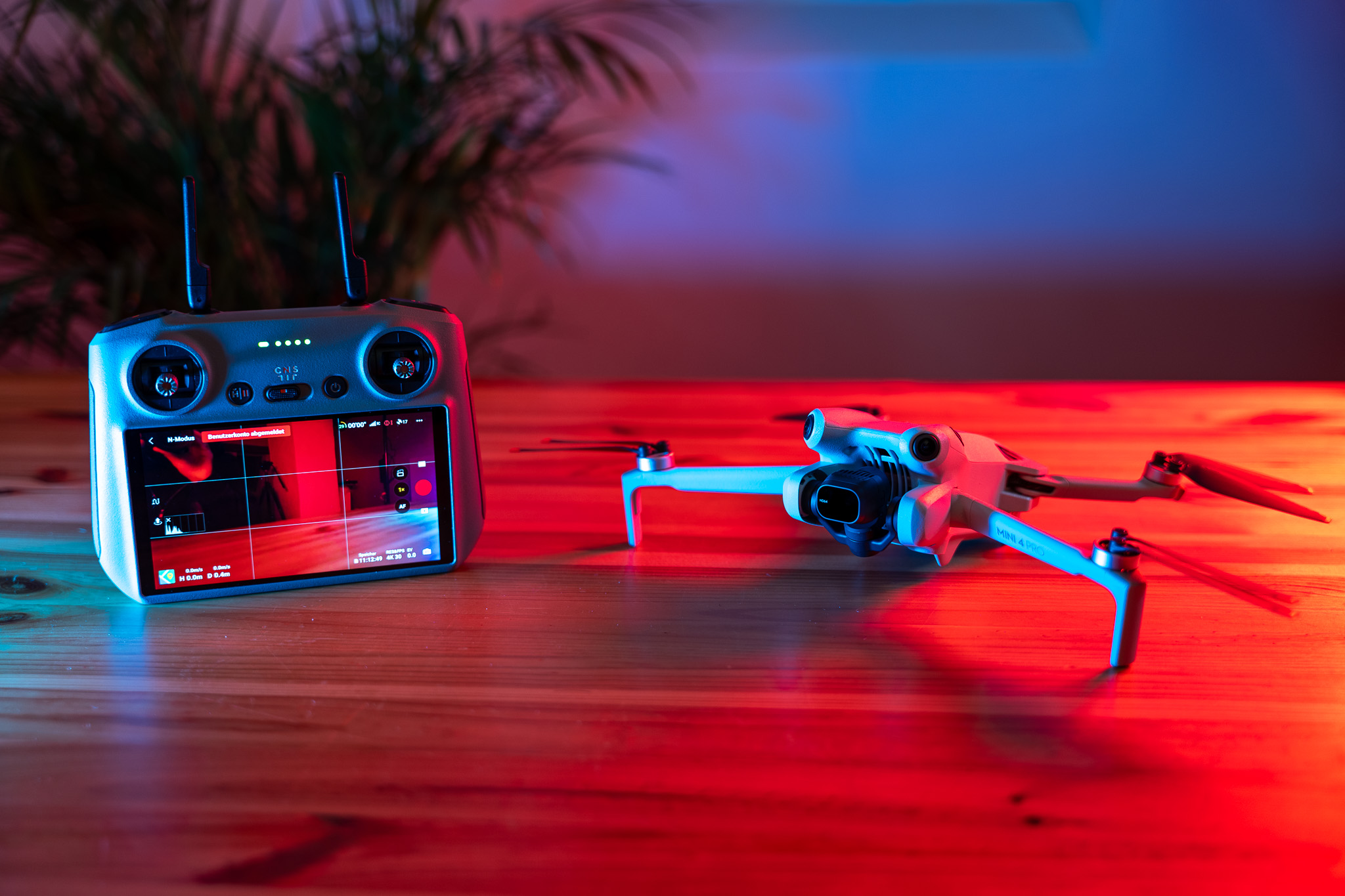 Eine Drohne mit vier Propellern auf einem Tisch, daneben eine Fernsteuerung mit Bildschirm, die Drohne zeigt an. Die Szene ist mit blauem und rotem Licht beleuchtet.
