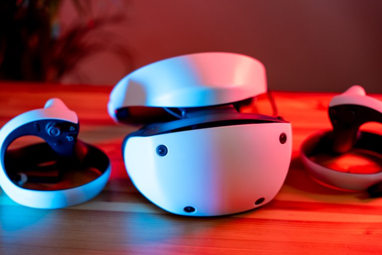 Ein modernes Virtual-Reality-Headset mit zwei Controllern, das auf einem Holztisch unter blauem und rotem Licht platziert ist.