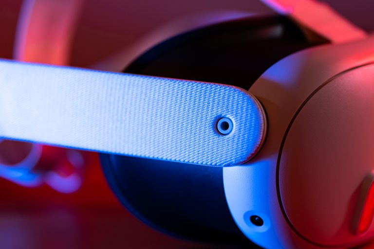 Nahaufnahme eines Virtual-Reality-Headsets mit weißem Kopfgurt, beleuchtet in blauem und rotem Licht.