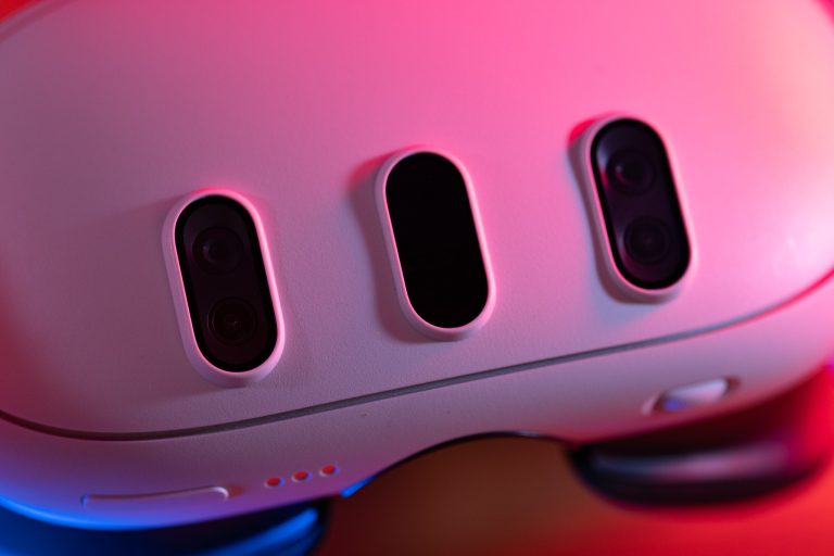 Nahaufnahme eines weißen Geräts mit drei Kameralinsen oder Sensoren, beleuchtet von pinken und blauen Lichtern. Es handelt sich um ein technisches Gadget, getestet von einem Technik-Blog.