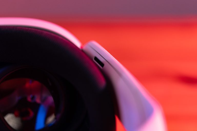 Nahaufnahme eines weißen VR-Headsets mit einer Linse im Vordergrund. Der Hintergrund ist orange-rot beleuchtet.