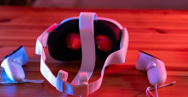 Ein Virtual-Reality-Headset auf einem Holztisch, umgeben von zwei Controllern. Die Szene ist in rotem und blauem Licht beleuchtet.