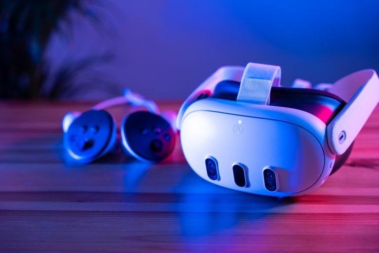 Nahaufnahme eines VR-Headsets und zwei Controllern auf einem Holztisch, beleuchtet von blauem und rosa Licht.